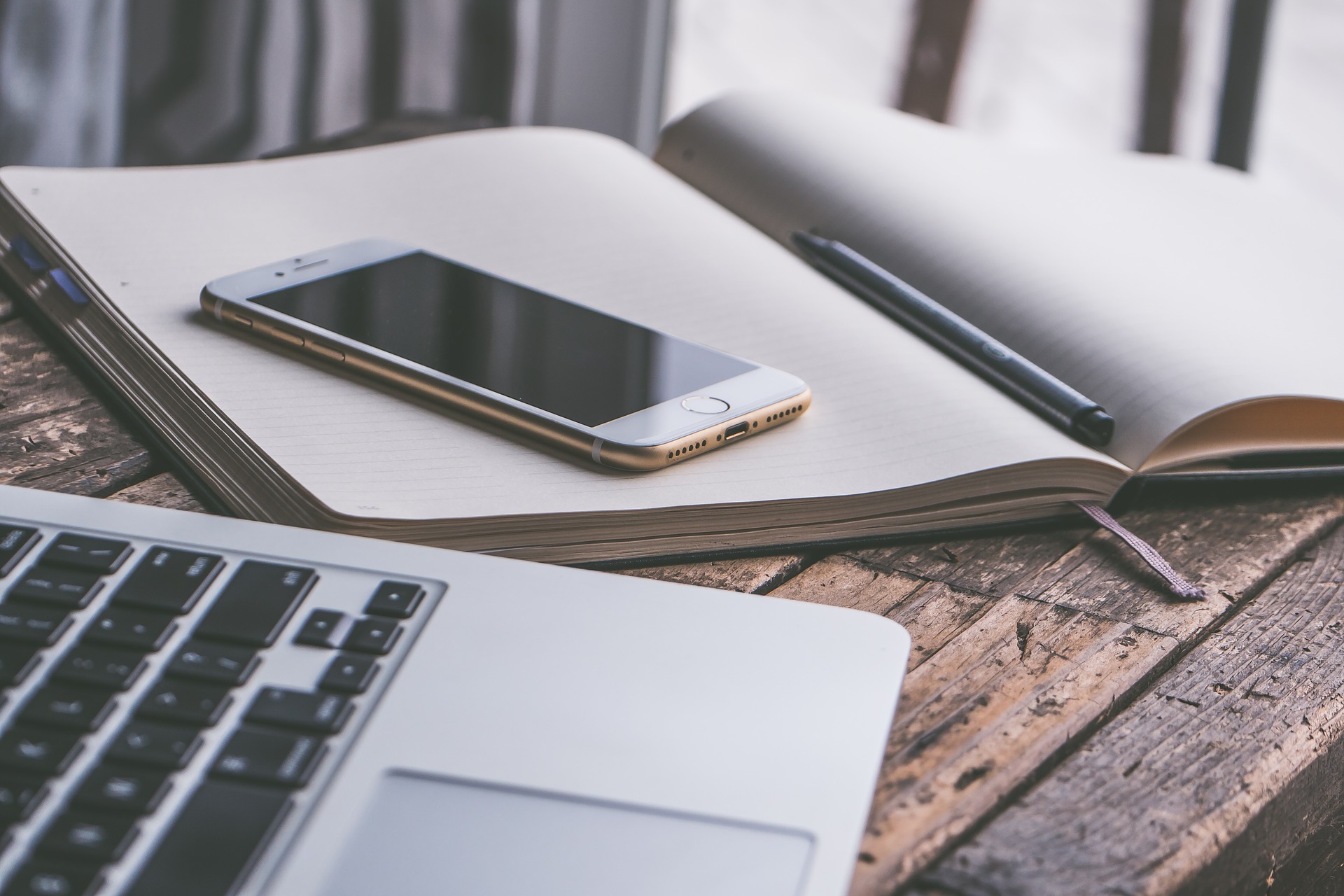 Photographie d'une bureau sur lequel reposent un ordinateur portable, un cahier ouvert avec un stylo et un téléphone portable